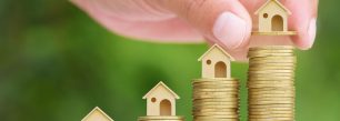 a person placing a house on top of a pile of coins.